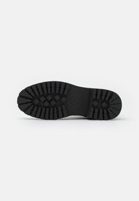 Suela de zapato de goma negra con profundos surcos, que muestra un patrón detallado para tracción. El diseño presenta una forma redondeada y una construcción robusta.