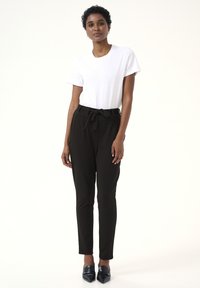 Černé kalhoty s vysokým pasem a uvázaným páskem, kombinované s bílým tričkem s kulatým výstřihem. Hladká textura, slim fit a délka ke kotníkům.