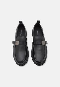 Sorte skinn loafers med en glatt overflate, med flat såle, dekorativ stropp og detaljer i metall foran. Kontraststing synlig.