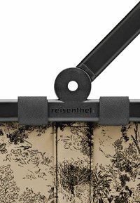 Carrello della spesa Reisenthel con manici in metallo neri e corpo in tessuto beige con motivo floreale. Chiusura sicura con dettagli neri.