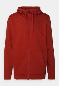 Red zip-up hoodie made of soft fabric, featuring a front zipper, two side pockets, and a black logo on the left chest. Adjustable drawstring hood.