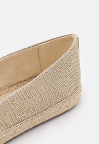 Chaussure espadrille en tissu beige tissé avec semelle en jute tressée et doublure intérieure lisse sur fond blanc.