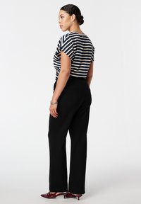 Gestreepte zwart-witte cropped shirt, zwarte wijde broek en rode puntige hakken. Haar in een bun gestyled, kijkt naar links.