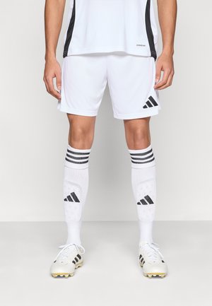 Maillot de sport blanc avec accents noirs, short assorti, chaussettes de football blanches avec rayures noires et un logo, et chaussures à crampons blanches.