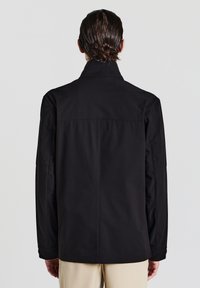 Giacca nera realizzata in materiale leggero e liscio. Presenta un alto colletto e un design con schiena dritta e maniche lunghe.