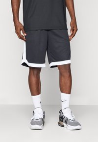 Pantalones cortos deportivos grises con detalle blanco, que cuentan con una textura suave y un diseño hasta la rodilla, combinados con zapatillas negras y blancas y calcetines de caña corta.