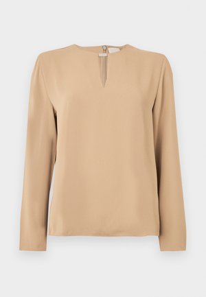 Beżowa bluzka z długim rękawem wykonana z gładkiego materiału. Posiada lekko wycięty dekolt w serek oraz zamek z tyłu z małą zawieszką. Prosty fason, bez wzorów.