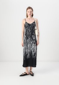 Zwart-witte jurk met spaghettibandjes, vloeiende stof en een knie-lange zoom. Gepaard met zwarte flats en een lichte handtas.
