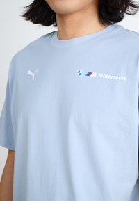Light blue cotton t-shirt featuring a white Puma logo and BMW Motorsport branding in blue, red, and white on the chest. Short sleeves.