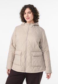 Beige quiltet jakke med hætte, der har lynlås foran, to store klaplommer og et tekstureret bølgemønster. Glat overflade.