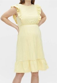 Abito giallo a lunghezza ginocchio con maniche arricciate, corpetto aderente e orlo a balze stratificate. Realizzato in tessuto morbido con una consistenza liscia.
