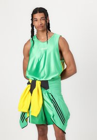 Echipament sportiv verde format dintr-un tricou fără mâneci și pantaloni scurți, cu accente negre și galbene. Materialul pare lucios și neted.