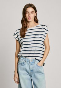 Striped cotton t-shirt in blue and white, round neckline, dropped shoulders. Worn with light blue jeans featuring studded accents.