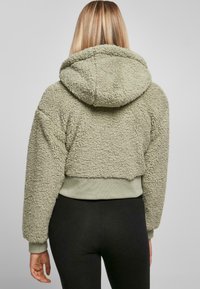 Kort hoodie i ljus olivgrön, gjord av mjukt, texturerat tyg. Har en huva och ribbade muddarmar, som ger värme och komfort.