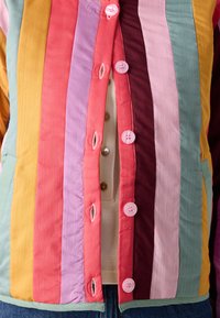 Mehrfarbige gestreifte Jacke mit knöpfbarem Frontverschluss. Verfügt über pinke, lila, grüne und gelbe Einsätze aus einem strukturierten, leichten Stoff.