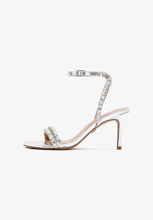 Silver high-heeled sandal with a slim ankle strap, embellished with rhinestones across the front. Smooth metallic texture and open toe design.