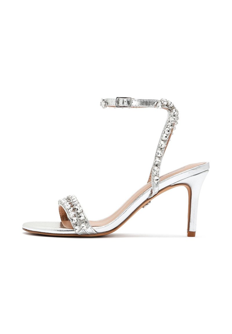 Sandal elegante con tacco alto in argento, dotato di una sottile cinghia alla caviglia, decorato con strass sul davanti. Texture metallica liscia e design con punta aperta.