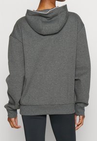 Harmaa hupullinen collegepaita kengurutaskulla, jossa on resorit helmassa ja hihoissa sekä näkyvä ommel hupun reunassa.