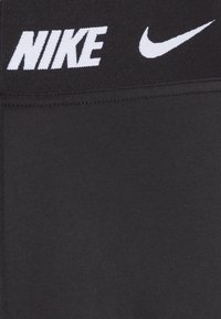 Černé sportovní legíny s hladkou texturou, s bílým logem „NIKE“ a symbolem swoosh na pasu. Jednoduchý, přiléhavý střih.