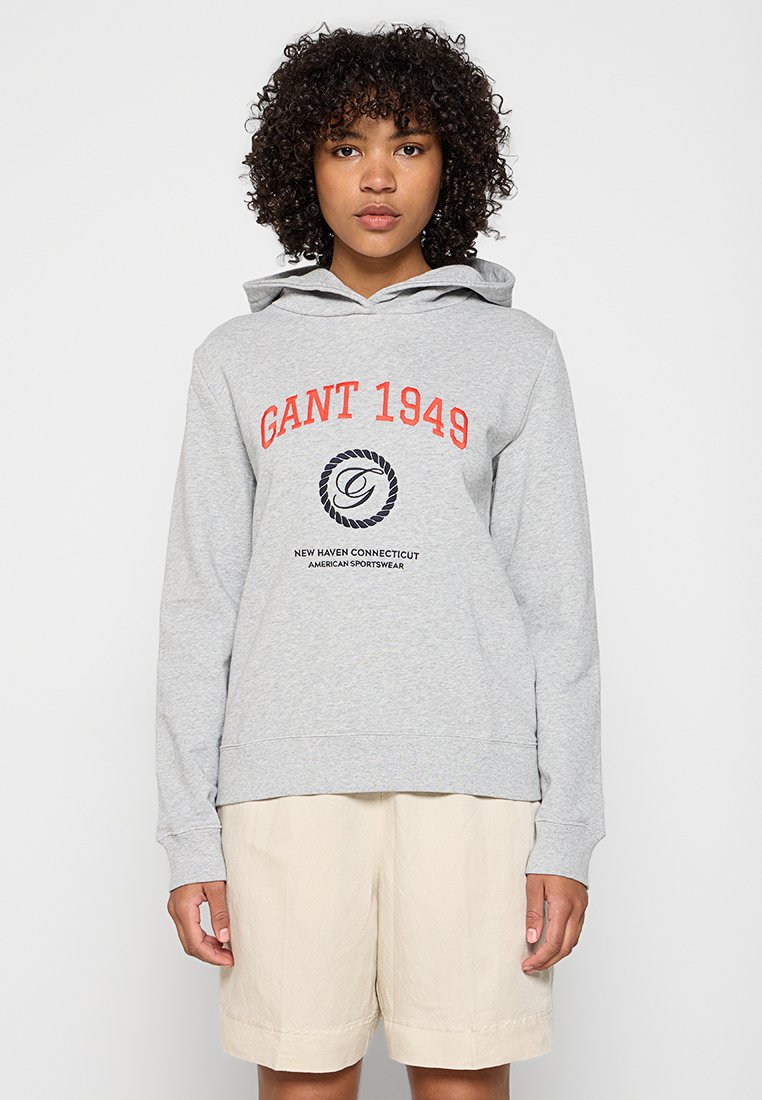 Grauer Hoodie aus Baumwollmischung, mit einem Front-Logo-Print in Rot und Blau, ausgestattet mit einer Kordelzugkapuze und gerippten Bündchen. Kombiniert mit beigen Shorts.