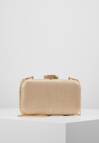 Bolso de mano dorado con acabado metálico, forma rectangular, superficie texturizada y una correa de cadena dorada. Cuenta con un cierre de clip en la parte superior.