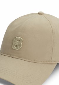 Beige baseball cap made of textured fabric, featuring an embroidered number "8" logo on the front. Curved brim with visible stitching details.