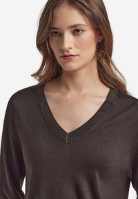 Mörkgrå v-ringad tröja med långa ärmar, med ribbad halslinning och slät yta. Fokus på modellens överkropp.