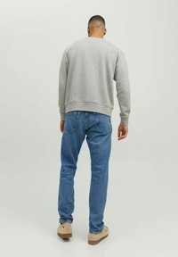 Grauer Pullover mit rundem Halsausschnitt, kombiniert mit blauen Jeans. Modell von hinten, um die gerippten Bündchen und den Taillenbund des Pullovers zu zeigen.