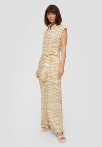 Leichter, ärmelloser, knöpfbarer Jumpsuit in Beige mit weißen Zebrastrifen. Verfügt über einen gebundenen Gürtel in der Taille und ein weit geschnittenes Bein-Design.