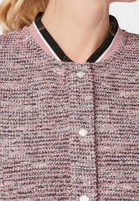 Strukturierte Jacke aus pinkem und mehrfarbigem Stoff mit einem schwarz-pinken gerippten Kragen, versehen mit silbernen Knöpfen entlang der Vorderseite.