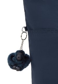Granatowa torba z tkaniny o teksturowanej powierzchni, z akcesorium w postaci puszystego breloka w kształcie goryla przymocowanego metalowym pierścieniem.