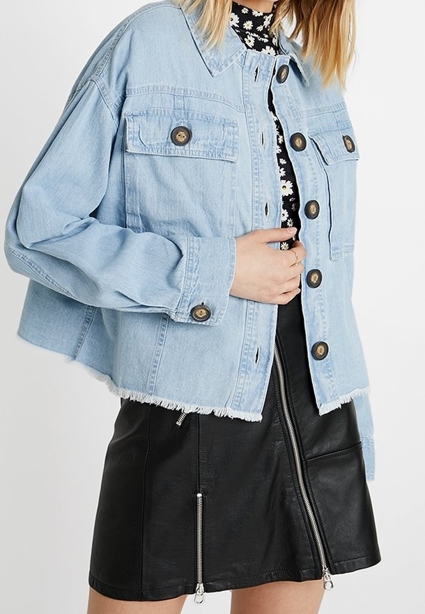 Světlemodrá denimová bunda s knoflíkovým zapínáním, dvěma náprsními kapsami a třepetajícím se lemem, spárovaná s černou koženou sukní s zipy.