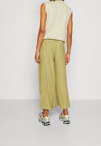 Ljusgröna vida byxor i strukturväv, tillsammans med en kortärmad beige topp och sportiga sneakers. Bakvy.