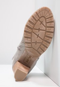 Bottine en suede grise avec une semelle en caoutchouc texturée de couleur marron clair. Présente des détails perforés et un talon en bois empilé.
