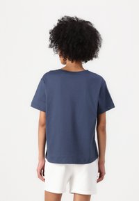 Marineblå bomulds t-shirt med korte ærmer og en rund halsudskæring. Bagsiden har en afslappet pasform og en lige kant, båret med hvide shorts.
