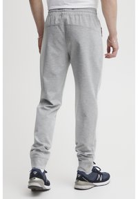 Gray sweatpants with a tapered leg, elastic waistband, textured fabric, and two back patch pockets. Paired with dark blue athletic shoes.