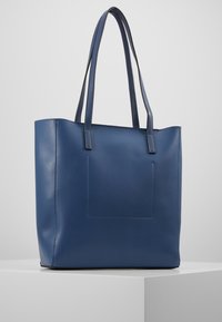 Niebieska skórzana torba typu tote z dwoma długimi uchwytami, prostokątnym kształtem, gładką teksturą i przednią kieszenią. Prosty design bez widocznych elementów montażowych.