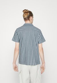 Modrá a bílá pruhovaná košile s krátkým rukávem a límečkem, s texturovanou tkaninou a volným střihem, z pohledu zezadu.