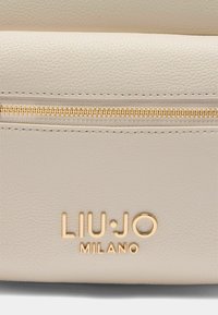 Hellbeige Handtasche aus strukturiertem Kunstleder, mit goldfarbener Reißverschluss und geprägt Logo-Text "LIU•JO MILANO."