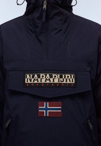Chaqueta de punto azul marino con cuello alto, cuenta con un bolsillo frontal, parche con el logo "Napa Pijri" y un parche de la bandera noruega. Tejido texturizado.