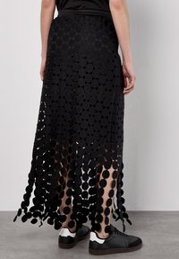Gonna maxy nera realizzata in tessuti circolari, con un design trasparente e vita elasticizzata, abbinata a sneakers in bianco e nero.