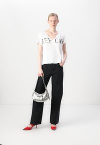 White V-neck T-shirt with "REPLAY" printed in black, paired with black high-waisted jeans; accessorized with a silver handbag and red heels.
