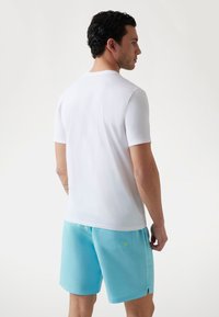 Hvid kortærmet t-shirt med rund hals, parret med lyseblå badebukser med sidelomme og en cirkulær detaljer.