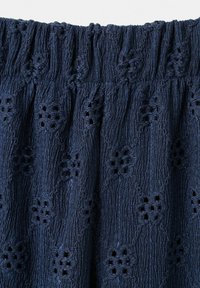 Tissu bleu marine avec taille élastique présentant un motif en chevrons texturé et des détails de broderie florale en découpe tout au long.