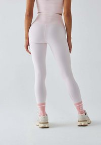 Jasnoróżowe legginsy z wysokim stanem o dopasowanym fasonie, w połączeniu z pastelowymi, prążkowanymi skarpetkami oraz masywnymi białymi sneakersami.