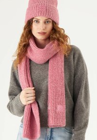 Pink knitted beanie and matching scarf with a ribbed texture, featuring a logo patch. The scarf is draped loosely, and both accessories are cozy.