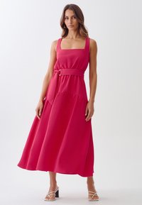 A sleeveless, square-neck, pink maxi dress with a belted waist, A-line silhouette, and layered bottom hem, made from a smooth fabric.