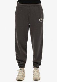 Pantalones de chándal grises con cintura y puños elásticos, con "USA" bordado en blanco en el muslo izquierdo. Tejido de algodón suave.