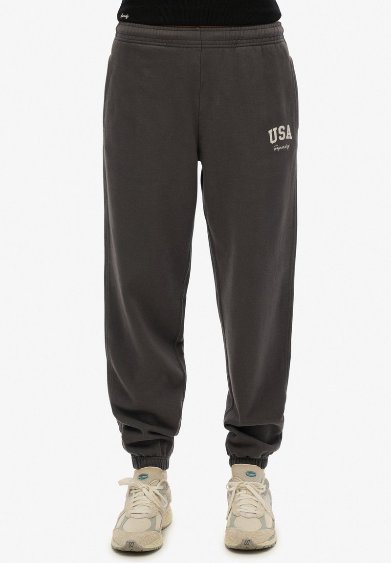 Pantalones de chándal grises con cintura y puños elásticos, con "USA" bordado en blanco en el muslo izquierdo. Tejido de algodón suave.