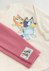 Felpa in tessuto crema con una grafica di cartone animato di due cani. Maniche rosa a coste con una toppa in tessuto che raffigura un cane e fiori.